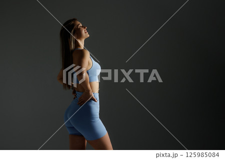 Fitness model posing confidently in workout attire against a dark backdrop emphasizing strength and determination 125985084