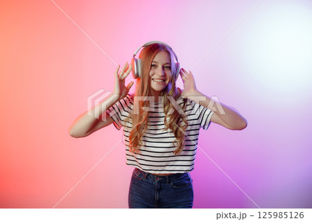 Young woman enjoys music with headphones in a colorful studio setting during a vibrant indoor photoshoot Young woman enjoys music with headphones in a colorful studio setting during a vibrant indoor photoshoot 125985126
