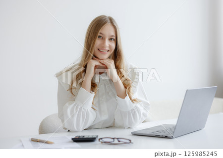 Young woman working at desk smiling with laptop during bright afternoon in minimalist workspace Young woman working at desk smiling with laptop during bright afternoon in minimalist workspace 125985245