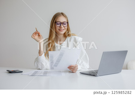 Young woman reviewing documents and planning finances at a modern desk in a bright office space Young woman reviewing documents and planning finances at a modern desk in a bright office space 125985282