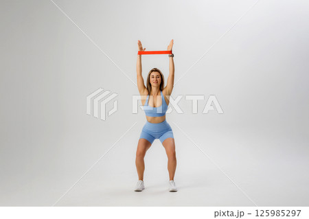 Woman performing resistance band exercise in workout attire during indoor training session Woman performing resistance band exercise in workout attire during indoor training session 125985297