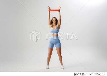 Woman performing a resistance band exercise for upper body strength in a bright studio Woman performing a resistance band exercise for upper body strength in a bright studio 125985298