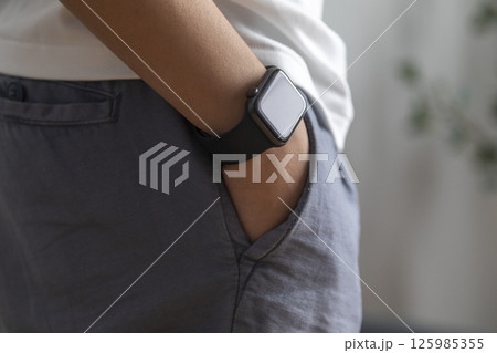 man putting his hand in his jeans pants pocket, wearing a smart watch. Technology. Trees on background. Smart gadget concept. 125985355