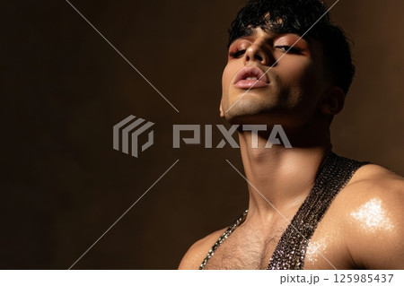 Bold pose of a fashion model showcasing striking makeup and glittering attire in a dramatic lighting setup during a photoshoot 125985437