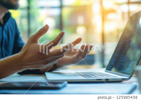 Person engaged in a discussion while using a laptop at a bright, modern workspace in the late afternoon 125985438