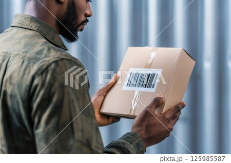 Man examines a brown package with a barcode in a modern shipping environment Man examines a brown package with a barcode in a modern shipping environment 125985587