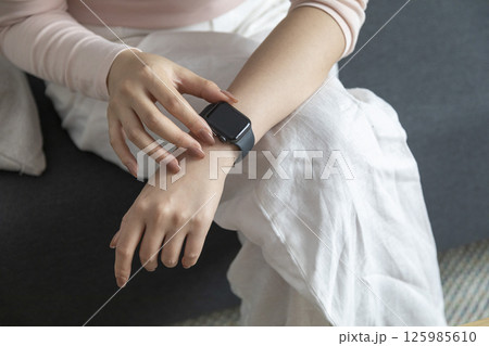 young woman using touchscreen smart watch sitting on sofa at Home. mixed race asian chinese model. young woman using touchscreen smart watch sitting on sofa at Home. mixed race asian chinese model. 125985610