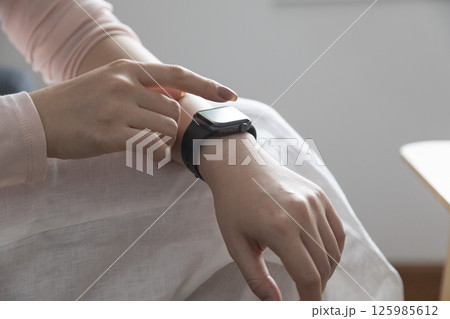 young woman using touchscreen smart watch sitting on sofa at Home. mixed race asian chinese model. 125985612