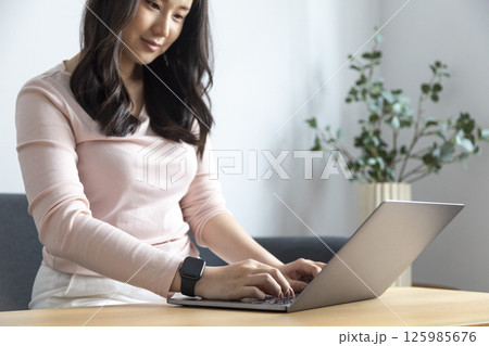 Work from home, Happy Asian young businesswoman use hand finger touch screen modern laptop computer she wears a smart watch on the wrist focus on smartwatch 125985676