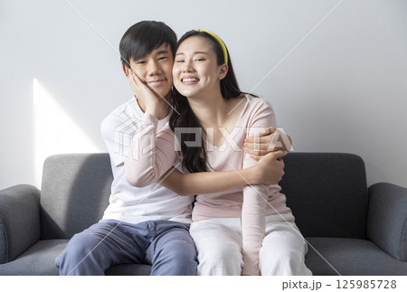 Laughing and hugging asian brother and sister with care and love on sofa at home. Laughing and hugging asian brother and sister with care and love on sofa at home. 125985728