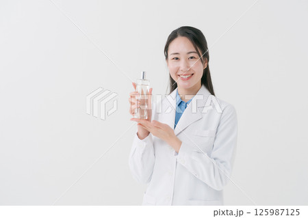 化粧水のボトルを持つ白衣の女性 化粧水のボトルを持つ白衣の女性 125987125