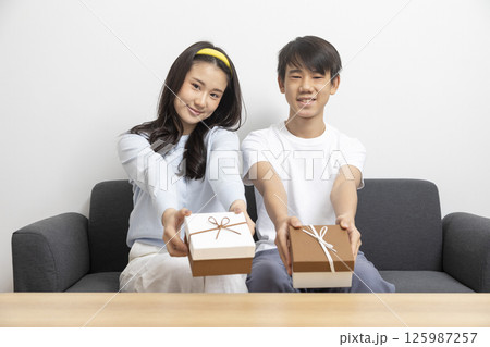 Excited, surprised woman receiving gift box from man sitting on a couch in the living room at home. Excited, surprised woman receiving gift box from man sitting on a couch in the living room at home. 125987257