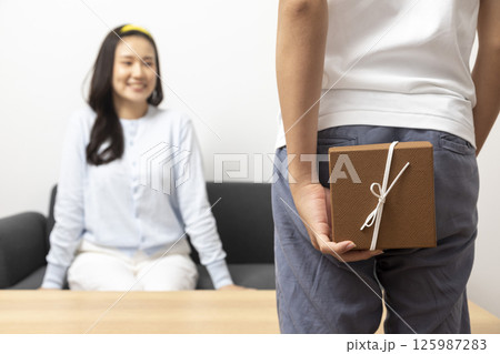 Guy is holding gift behind him is trying to surprise his is waiting girlfriend at home. Focus on boy. Guy is holding gift behind him is trying to surprise his is waiting girlfriend at home. Focus on boy. 125987283