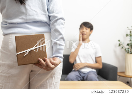 Guy is holding gift behind him is trying to surprise his is waiting girlfriend at home. Focus on boy. 125987289