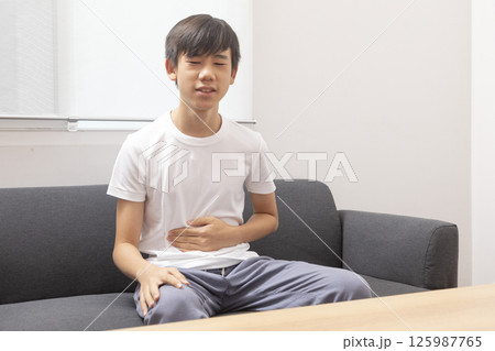 eautiful boy wearing casual  t-shirt at home with hand on stomach because indigestion, painful illness feeling unwell. Ache concept. 125987765
