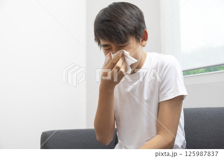 healthcare, rhinitis, people and medicine concept - ill boy with flu lying in bed and blowing his nose at home healthcare, rhinitis, people and medicine concept - ill boy with flu lying in bed and blowing his nose at home 125987837