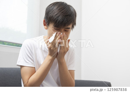 healthcare, rhinitis, people and medicine concept - ill boy with flu lying in bed and blowing his nose at home healthcare, rhinitis, people and medicine concept - ill boy with flu lying in bed and blowing his nose at home 125987838