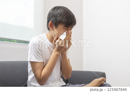 healthcare, rhinitis, people and medicine concept - ill boy with flu lying in bed and blowing his nose at home 125987840