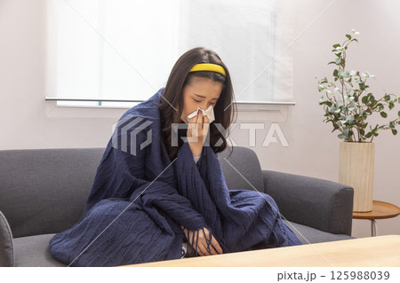 girl is sitting at sofa and working remotely on laptop. Female is blowing out snot, having fever and headache. Young woman is treated at home, took sick leave. Winter cold and flu concept girl is sitting at sofa and working remotely on laptop. Female is blowing out snot, having fever and headache. Young woman is treated at home, took sick leave. Winter cold and flu concept 125988039
