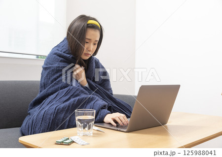 girl is sitting at sofa and working remotely on laptop. Female is blowing out snot, having fever and headache. Young woman is treated at home, took sick leave. Winter cold and flu concept girl is sitting at sofa and working remotely on laptop. Female is blowing out snot, having fever and headache. Young woman is treated at home, took sick leave. Winter cold and flu concept 125988041