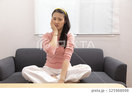 Asian young woman sitting on the sofa at home touching mouth with hand with painful expression because of toothache or dental illness on teeth. dentist 125988098