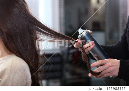 Hair spray in hands of hairdresser. Hairdresser at beauty salon styles woman's hair into curls using hair spray. Hairstyle with curls. Lock of hair in close-up. Concept of beauty. 125988335