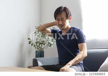 Upset mid adult man suffering from neck pain on sofa at home Upset mid adult man suffering from neck pain on sofa at home 125988663