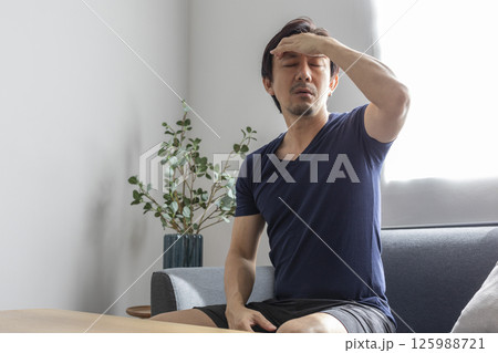 Upset sick stressed young caucasian man in casual clothes sits on sofa in the living room, bending over, massaging his head, suffering from pain, migraine, closing his eyes, needs treatment and rest 125988721