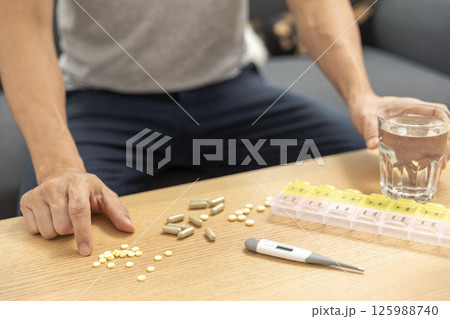 Young Asian man feeling sick and taking pills while sitting on the bed at home with medicines tablets and drinking water on table. Healthcare and Medicine concept Young Asian man feeling sick and taking pills while sitting on the bed at home with medicines tablets and drinking water on table. Healthcare and Medicine concept 125988740