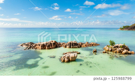 Massive granite rocks rest in shallow, turquoise waters, blending into the tropical landscape. 125988799