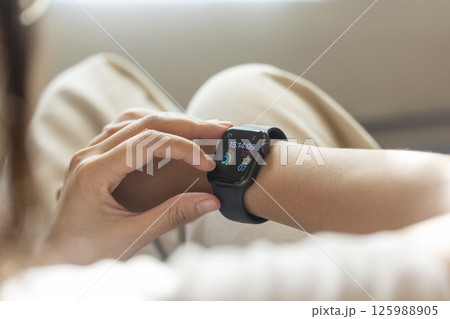 young woman using touchscreen smart watch sitting on sofa at Home. mixed race asian chinese model. 125988905