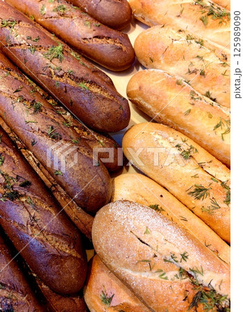 freshly baked bread loaves with herbs displayed on wooden surface in bakery setting. 125989090