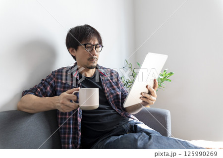 Happy asian young adult man sitting on sofa at living room reading fiction book. Domestic life relax at home. 125990269
