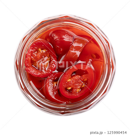 Pickled red jalapeno slices, in an open screw-top glass jar, isolated, from above. Medium-sized hot, red chili peppers, cut into cross sections, pasteurized and preserved in a salted vinegar brine. 125990454