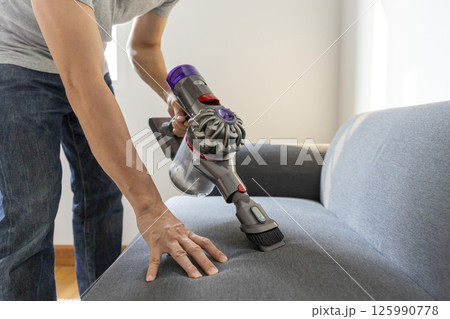 Adult Man in jeans and T-shirt vacuuming a sofa 125990778