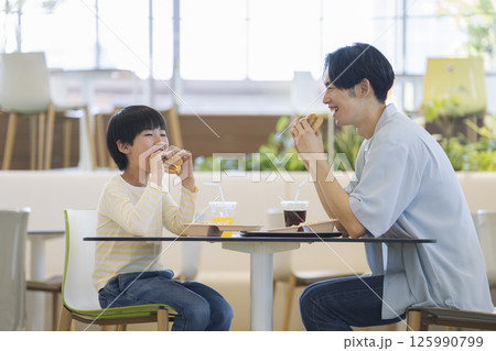 向かい合ってハンバーガーを食べる親子　9歳の男の子と30代の父親 125990799