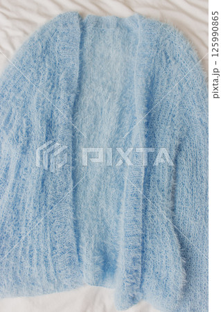 Blue knitted cardigan on white background. Soft blue knitted sweater in details. Knitting pattern background. Summer knitted fashion. Cozy hobby. Craft product concept. Blue knitted cardigan on white background. Soft blue knitted sweater in details. Knitting pattern background. Summer knitted fashion. Cozy hobby. Craft product concept. 125990865
