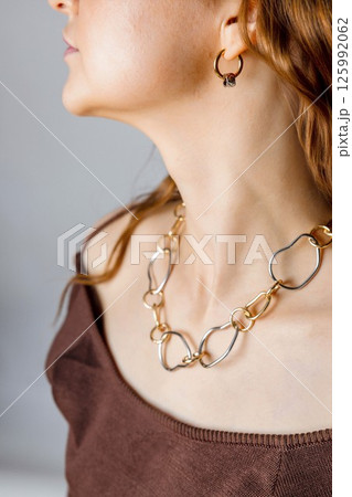 closeup of woman wearing abstract chain necklace, gold earrings, jewelry on exposed collarbones and bare shoulders with red wavy hair, accessories brand, jewelry design, luxury fashion 125992062