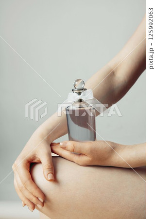 woman hold glass perfume bottle with white bow on neutral background, gentle hand positioning, natural nails, beauty branding, skincare marketing, luxury fragrance, vertical woman hold glass perfume bottle with white bow on neutral background, gentle hand positioning, natural nails, beauty branding, skincare marketing, luxury fragrance, vertical 125992063