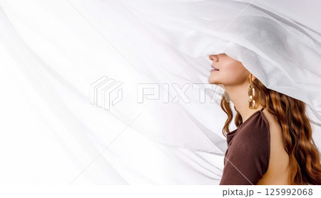 woman with long wavy red hair and golden earrings smiling under white sheer fabric in brown open-back dress, feminine mood in studio, jewelry design, beauty editorial, web banner woman with long wavy red hair and golden earrings smiling under white sheer fabric in brown open-back dress, feminine mood in studio, jewelry design, beauty editorial, web banner 125992068