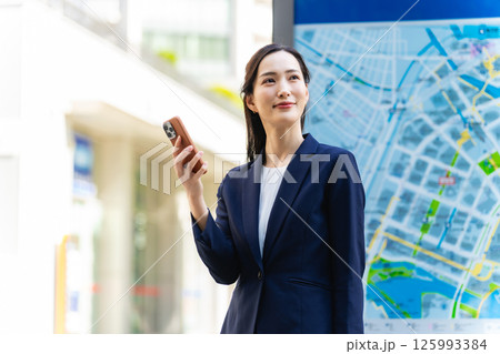 地図とスマホを見て場所を確認する女性ビジネスパーソン 125993384