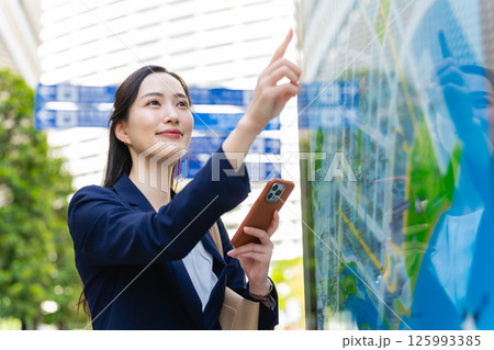地図とスマホを見て場所を確認する女性ビジネスパーソン 125993385