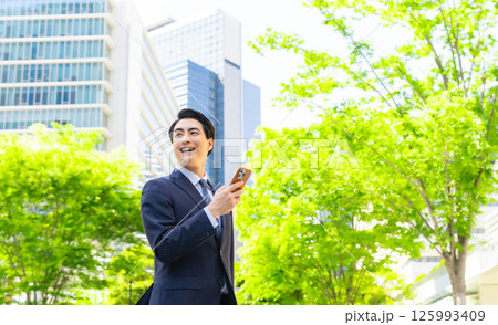 新緑の街でスマホを使う男性ビジネスパーソン 125993409