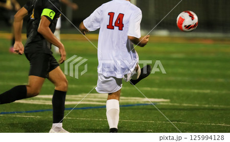 Player Kicks Soccer Ball During Match at a night game under the lights Player Kicks Soccer Ball During Match at a night game under the lights 125994128