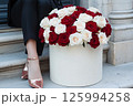 A luxurious bouquet of red and white roses is in a decorative gift box beside a stylishly woman legs in sparkly shoes. Valentines Day, flower store, shop, mock-up, delivery flowers, blog posts 125994258