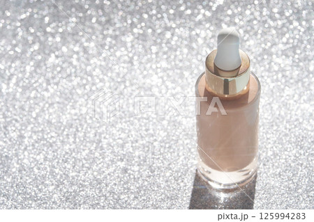 Shimmering bottle of skincare serum with dropper on sparkling glitter background Shimmering bottle of skincare serum with dropper on sparkling glitter background 125994283
