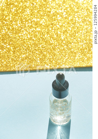 Cosmetic serum bottle on blue surface with sparkling gold background 125994284
