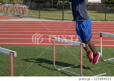 Athlete Performs Hurdle Training on Track Field in Sunny Weather 125994521