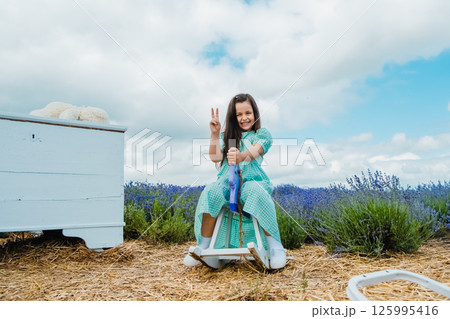 Wooden rocking horse toy in a lavender field. Beautiful girl riding a toy rocking horse.  125995416