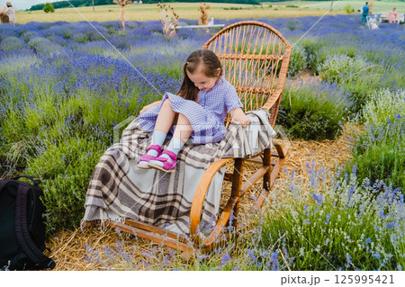 A girl with long, loose hair and a purple dress is sitting in a rocking chair in a lavender field. A girl with long, loose hair and a purple dress is sitting in a rocking chair in a lavender field. 125995421